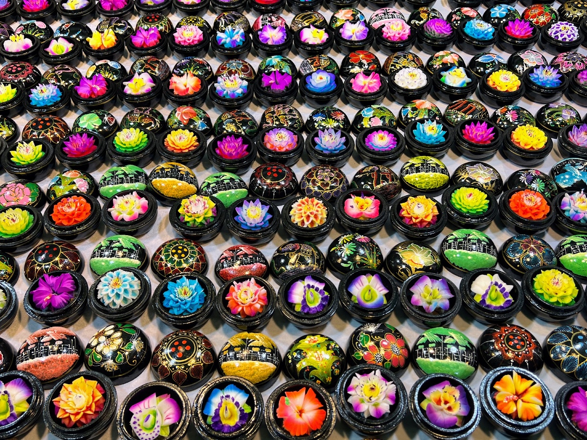 Many rows of brightly colored and intricately hand-carved soaps on display in small round wooden containers, the lids of which are also painted brightly.