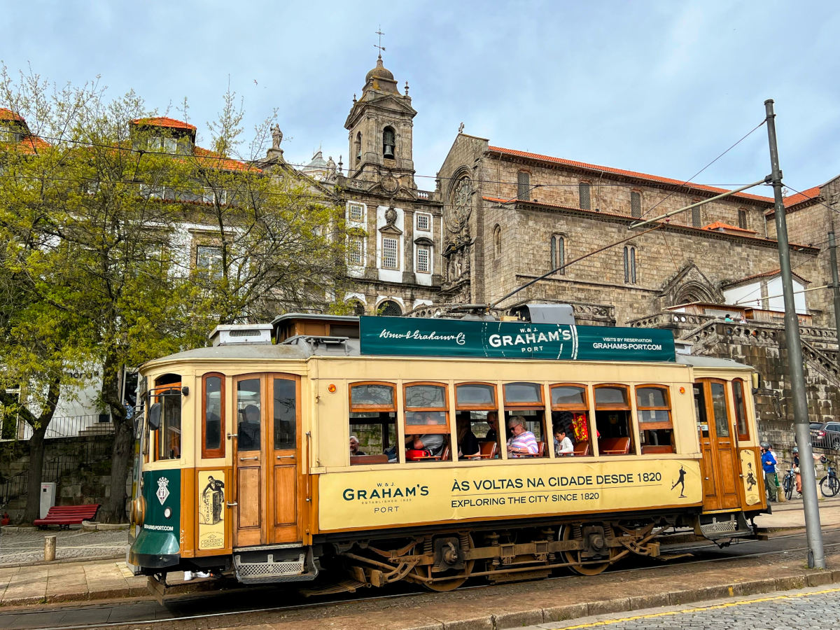 Pale yellow and wooden tram carrying passengers through the Old Town in Porto.