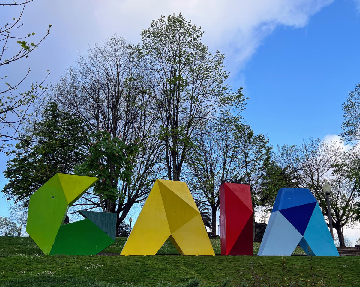 In a park setting, giant characters spelling GAIA stand in green, yellow, red, and blue lettering.