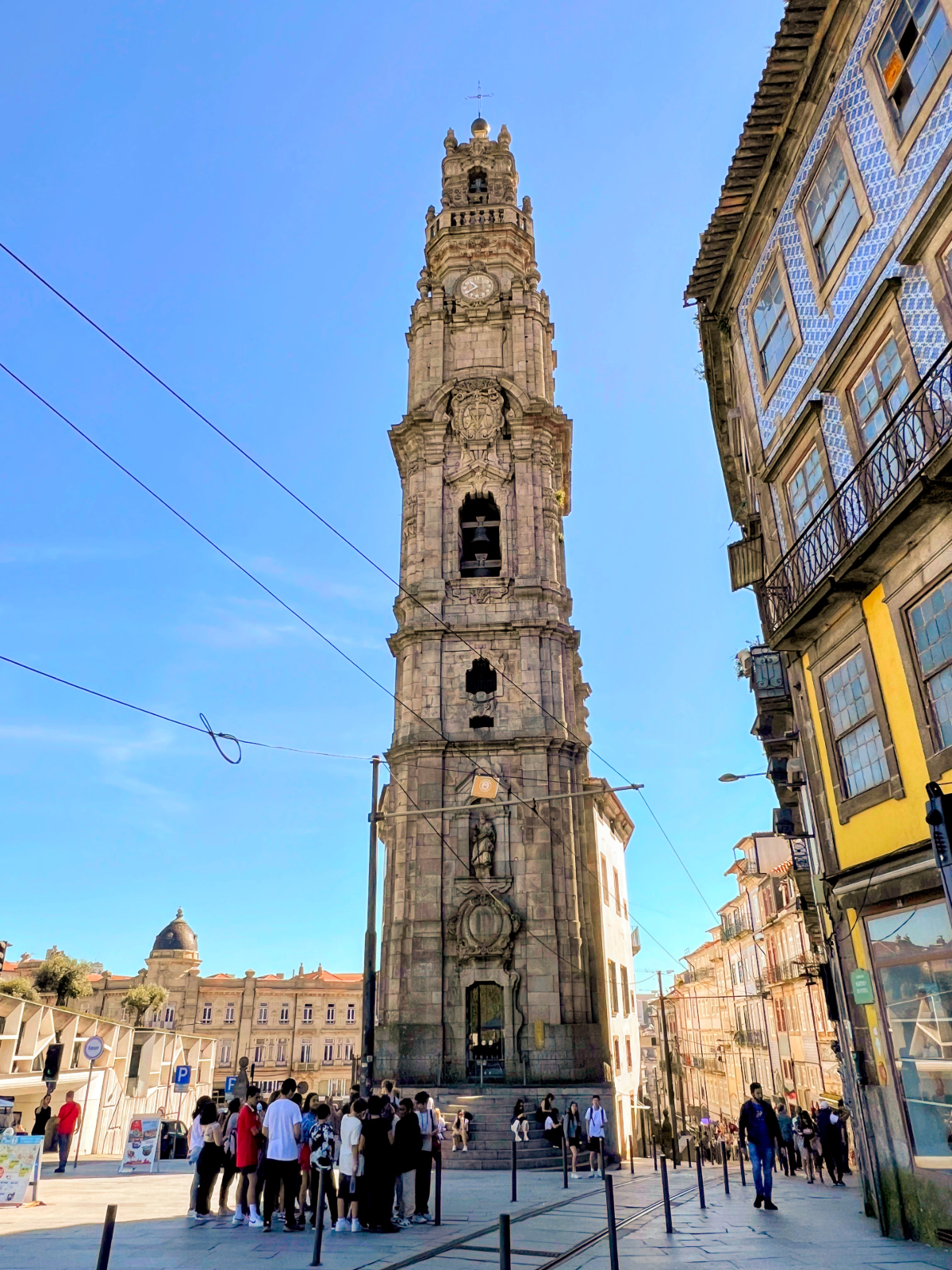 Under a cloudless blue sky, the Clerigos Church tower looms over street, dwarfing the crowds of people standing at the bottom.