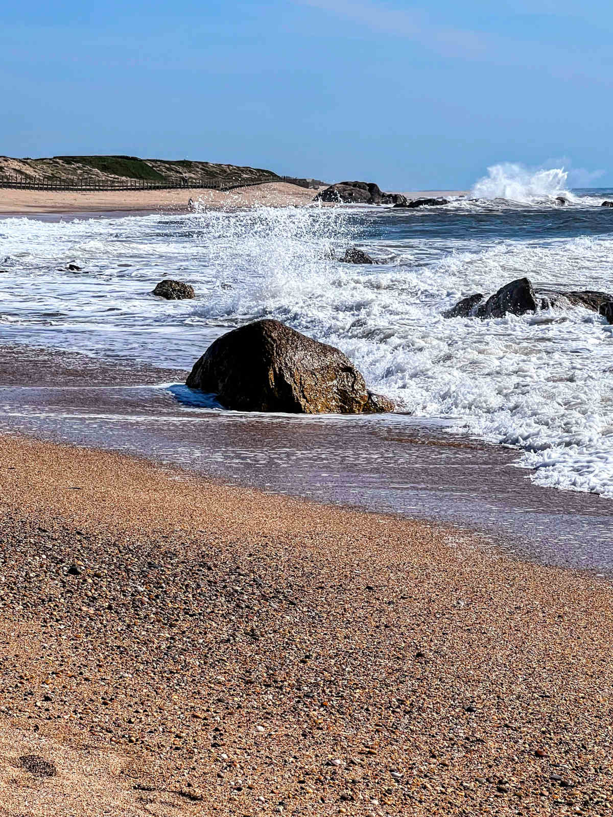 Portrait view of the seaside - sand, some rocks in the ocean, and the white water of crashed waves.