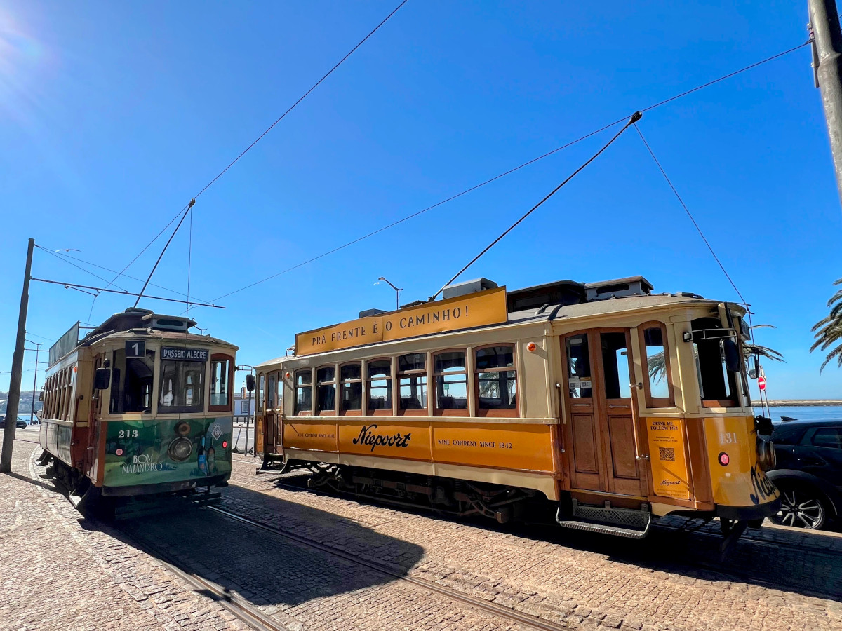 Two trams - one green and one yellow-orange - sitting next to one another under an azure blue sky.