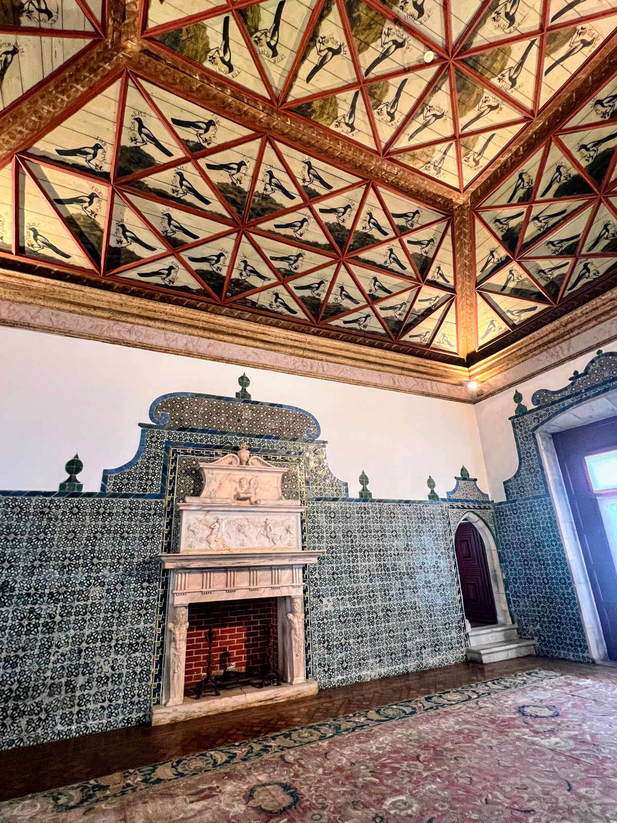 Portrait featuring intricately painted palace ceiling of 136 magpies, tiled walls, and rich red tapestry carpet.