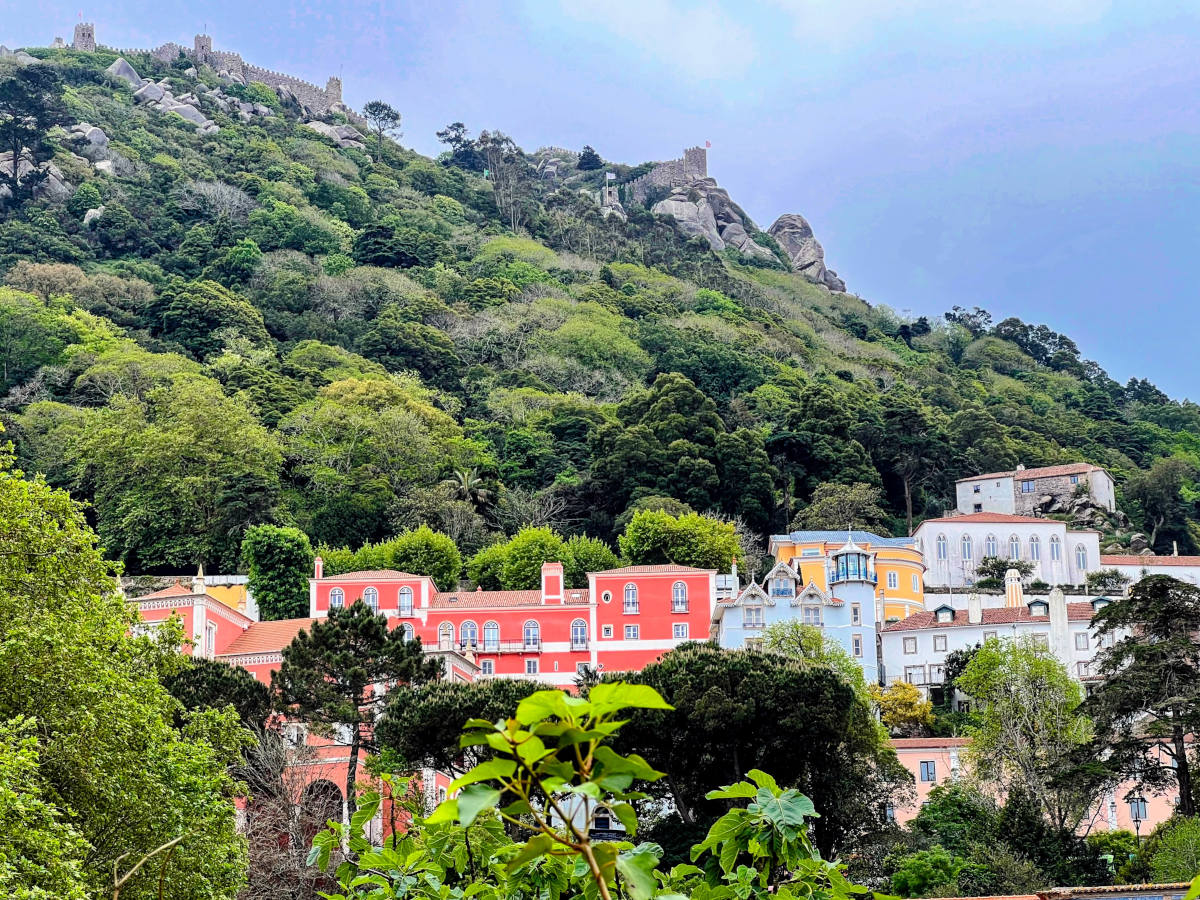 An old Moorish castle wall looms atop a far hill overlooking the colourfully painted buildings nestled into the hillside town of Sintra Portugal.