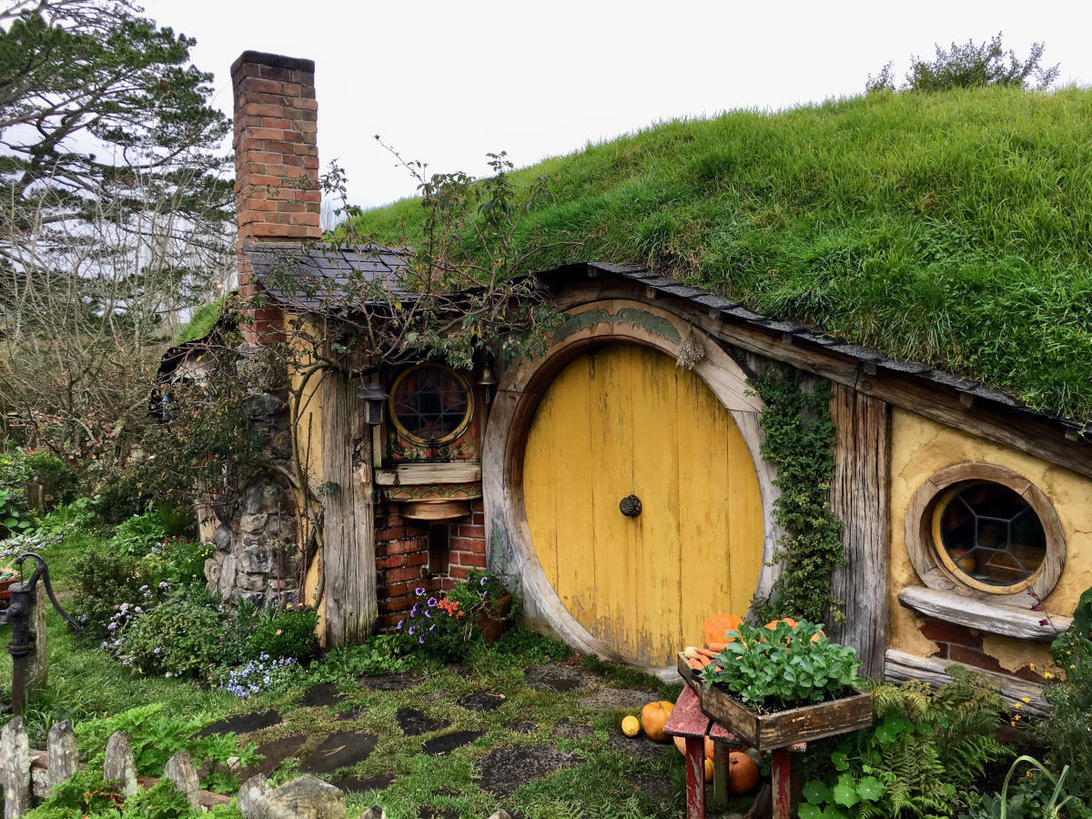 Tiny Hobbit house with yellow, circular wooden door built into a green hillside.