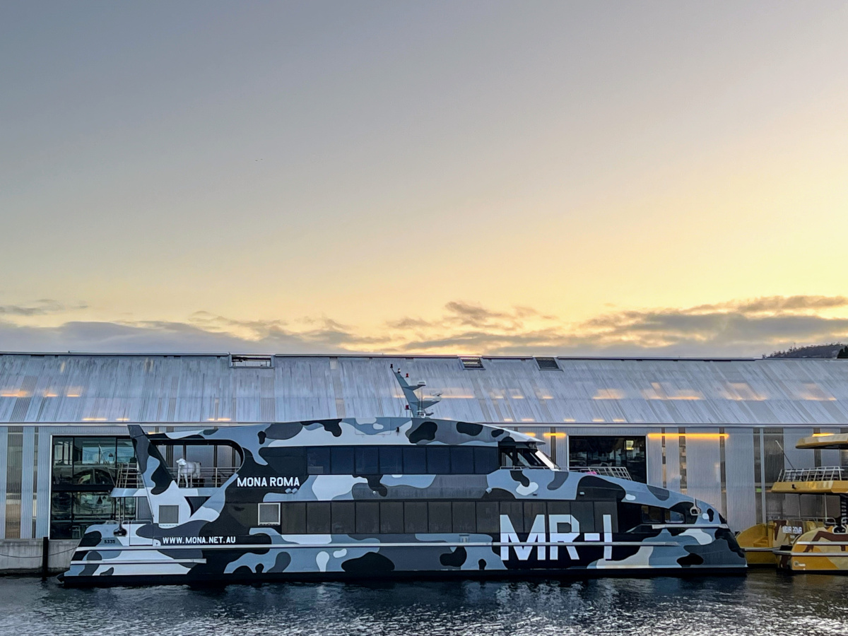 Landscape image of grey-shade camouflage painted passenger ferry in front of a grey dockside building at sunset in Hobart - a great thing to do in Hobart!
