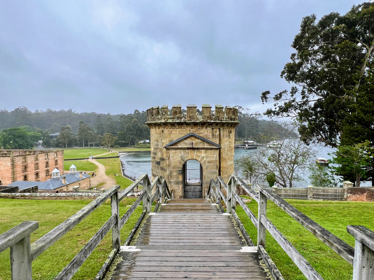Landscape scene from wooden walkway towards an old circular sandstone tower in the mid-ground and cove in the background.