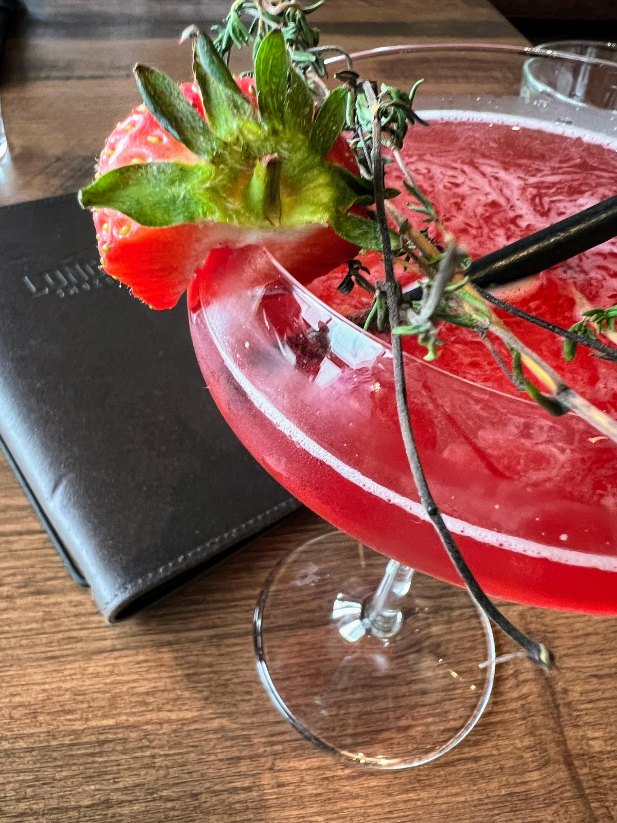 Looking down on a red cocktail with a strawberry and rosemary garnish.