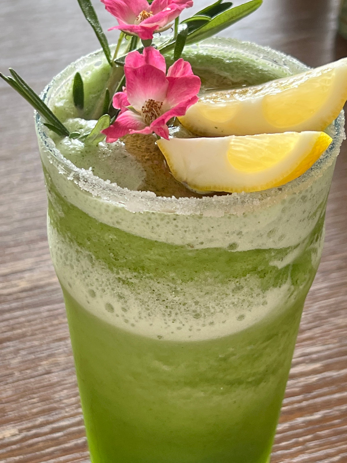 Green cocktail with two lemon wedges and a pink flower in the top.