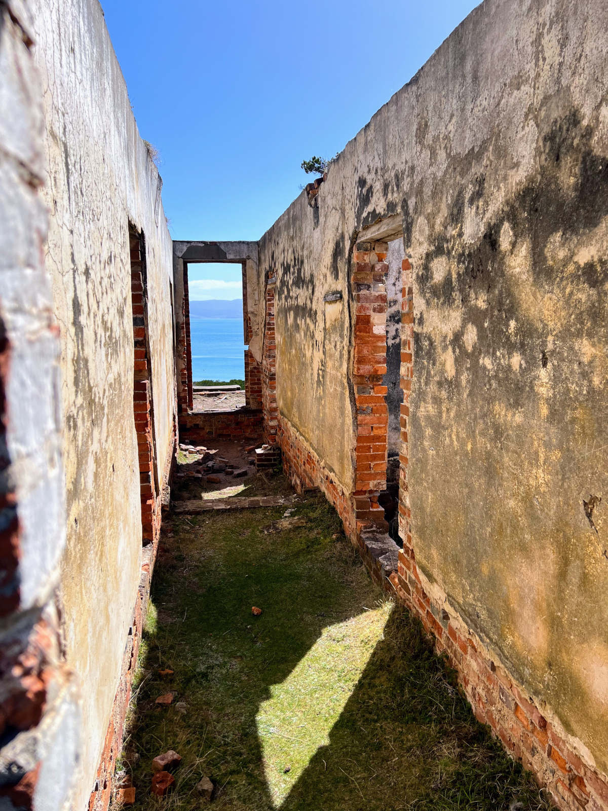 Portrait view looking through brick building ruins to blue sea beyond on Maria Island, Tasmania.
