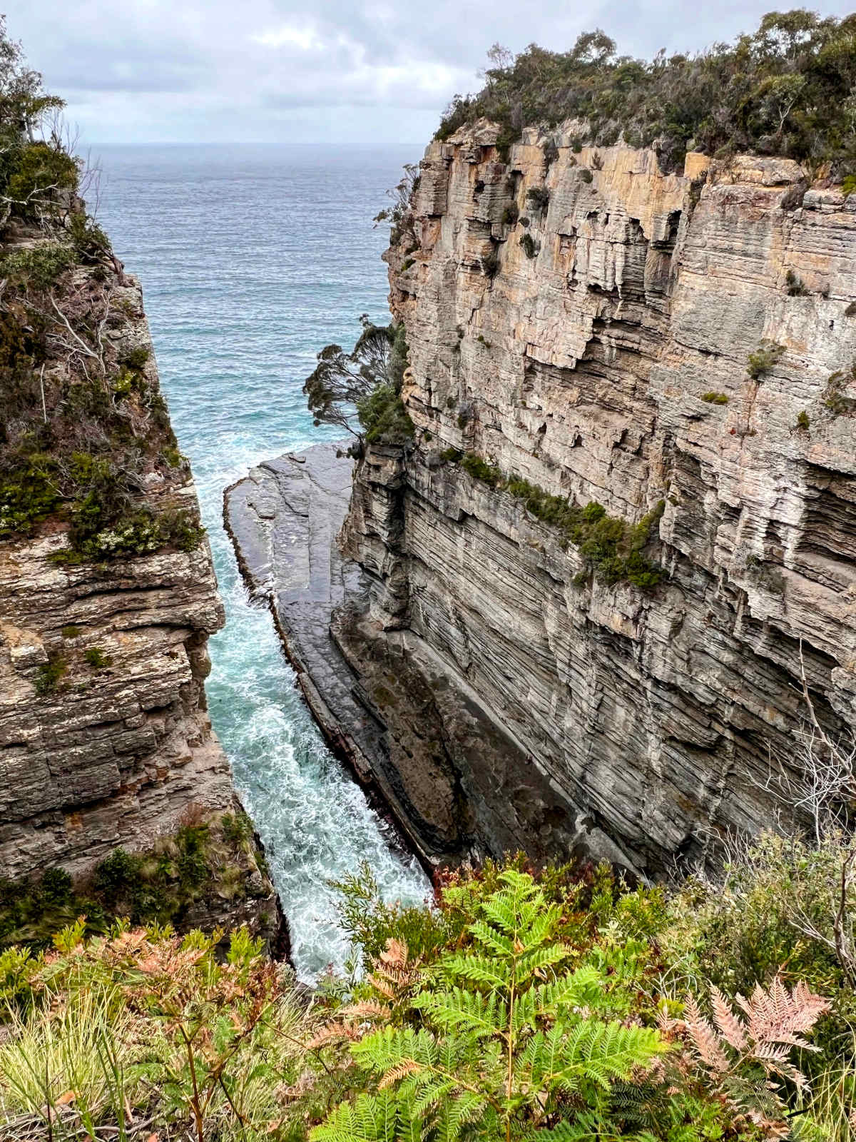Portrait view of a steep rocky chasm with the ocean in the background.